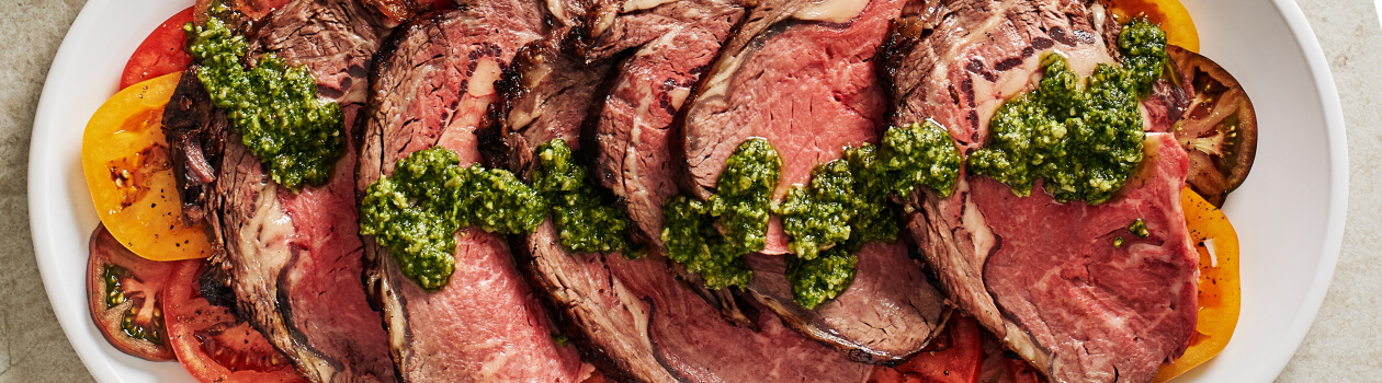 Sliced prime rib roast with pesto drizzled on top.