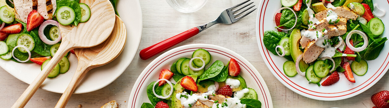Overhead shot for Strawberry and Chicken Spinach Salad in two plates with dressing and torn baguette on the side.